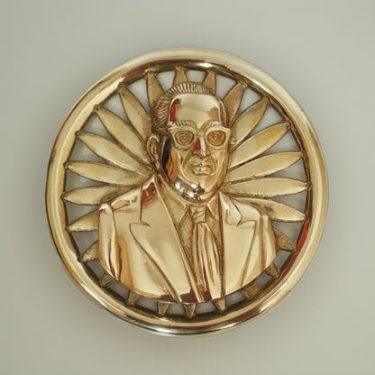 Gold medallion with a portrait of a person wearing sunglasses and a suit, surrounded by sunburst design.