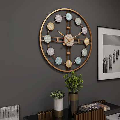 Decorative wall clock with colorful accents on a dark gray wall, with a plant and framed picture in the foreground.