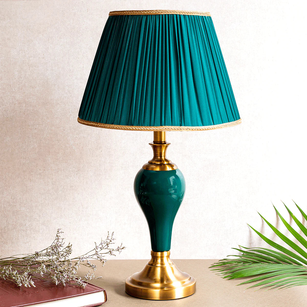 Table lamp with teal pleated shade and gold base on a neutral background