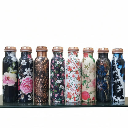 Decorative bottles with floral and abstract designs on a reflective surface.
