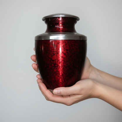 Red metallic urn held in a hand against a gray background