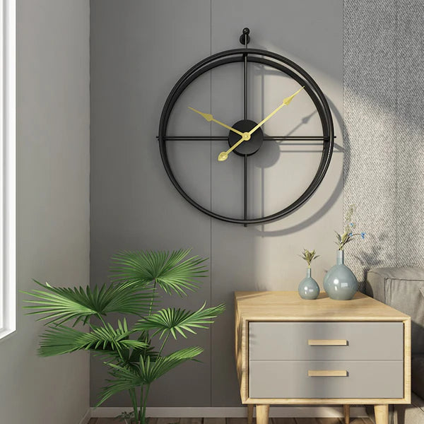 Decorative wall clock on a gray wall with a side table and plant in the foreground.