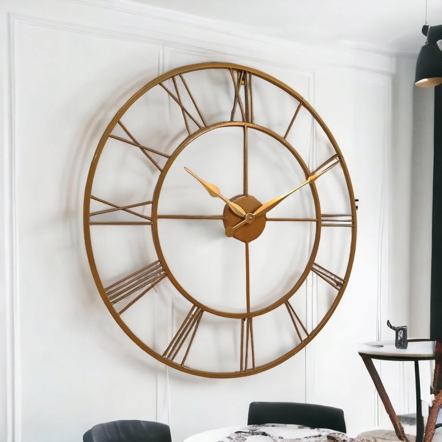 Large gold wall clock on a white wall with a dining table and chairs in the background.