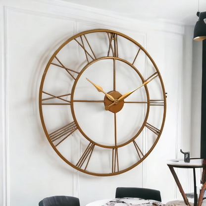 Large gold wall clock on a white wall with a dining table and chairs in the background.